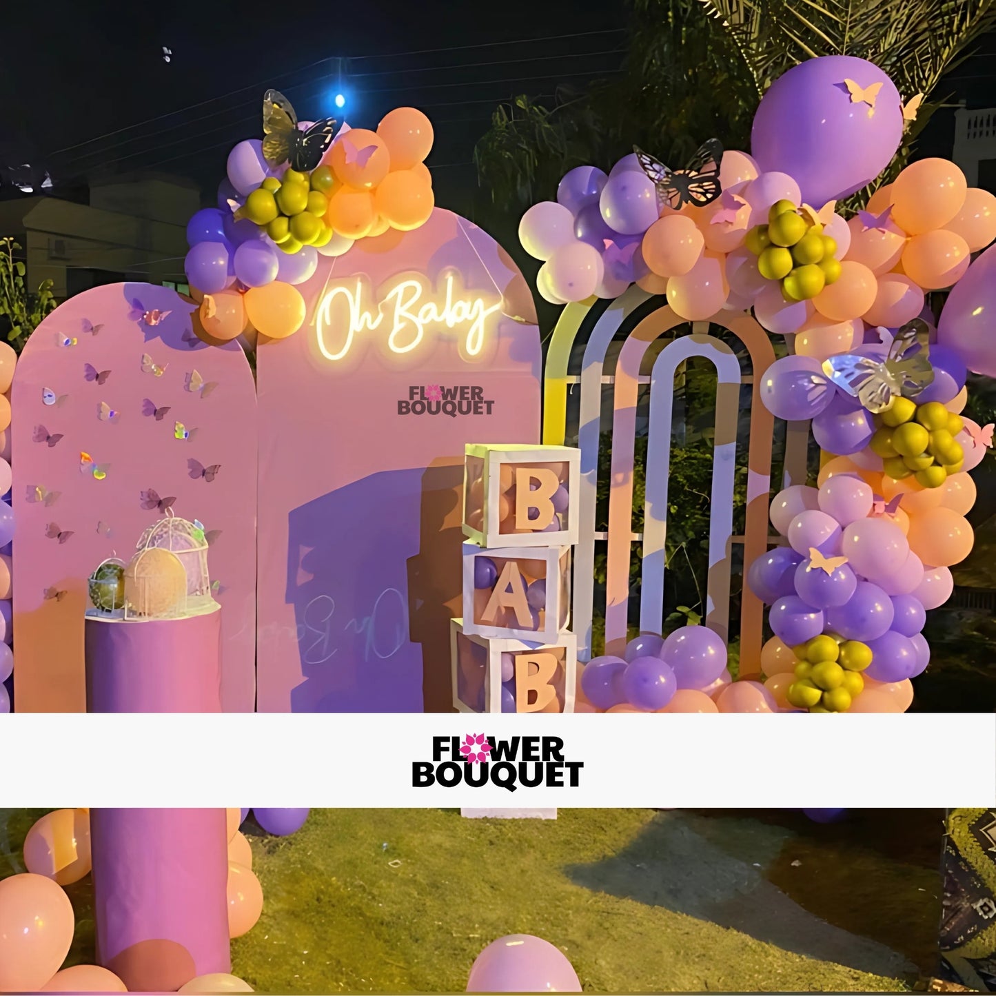 Beautiful baby shower decoration with a vibrant balloon arch in purple, pink, and yellow, adorned with butterfly decorations, a neon 'Oh Baby' sign, and stacked 'BABY' blocks, creating a joyful and festive atmosphere.