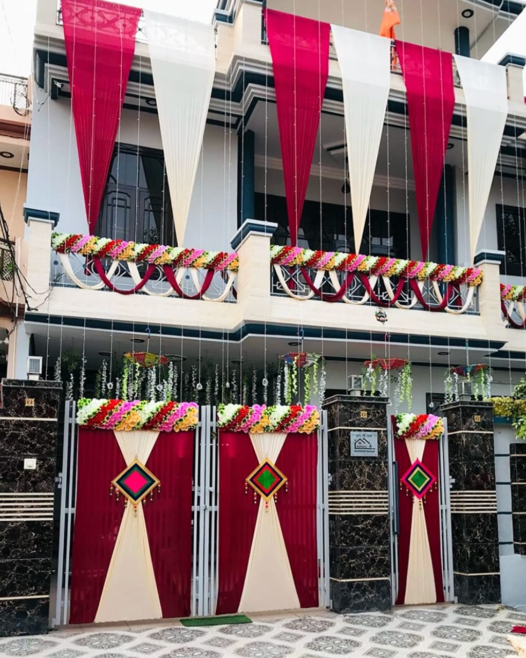 Gate and balcony draped with red and white fabric, decorated with colorful floral garlands.