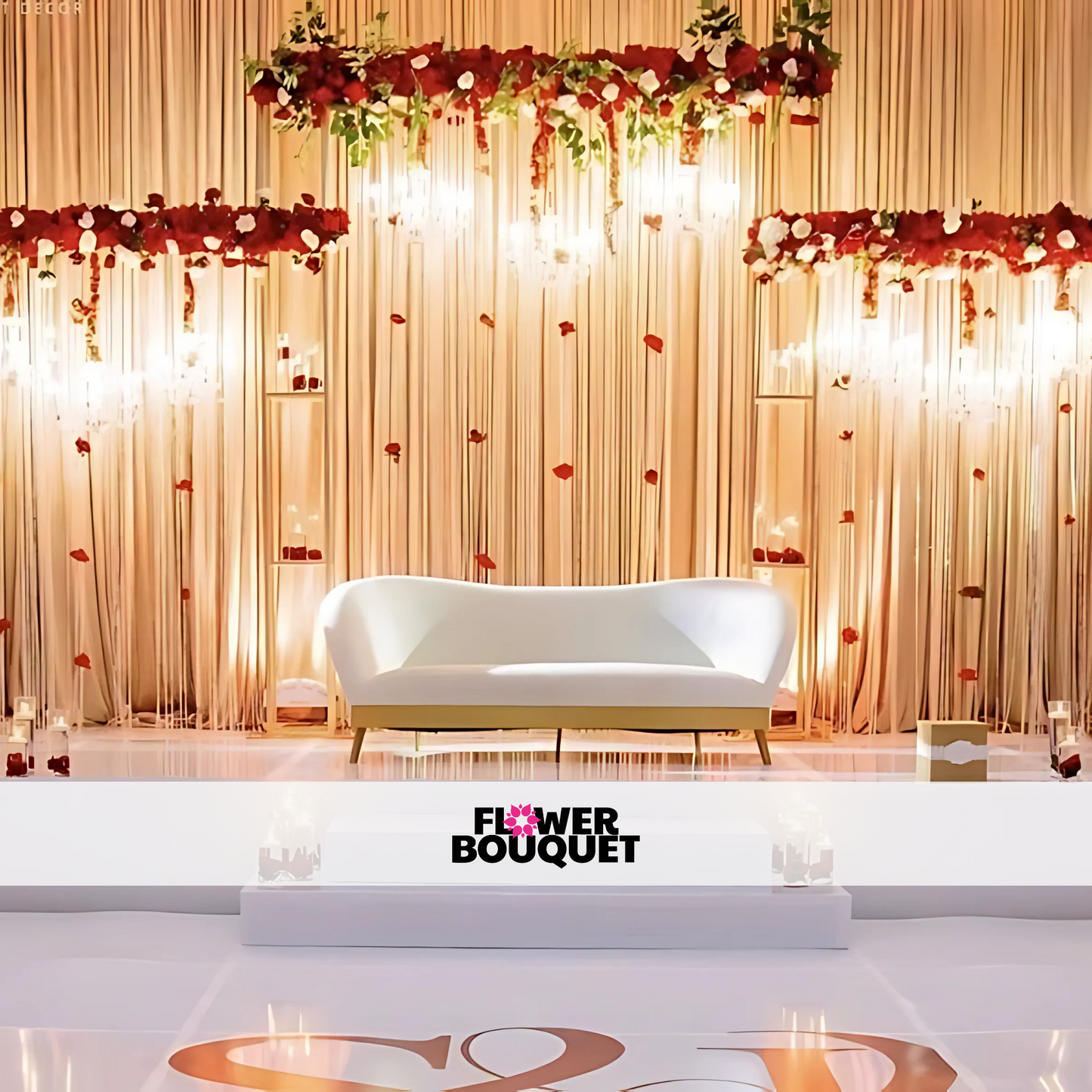 Wedding stage with a minimalist white sofa, gold drapery backdrop, cascading red flowers, and warm lighting, perfect for elegant celebrations.