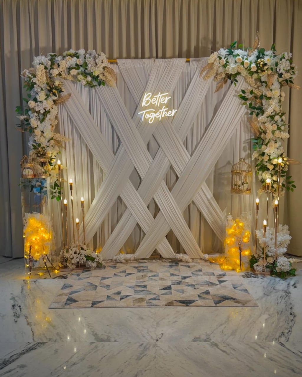 White backdrop with crisscross drapes, floral decor, and soft lighting.