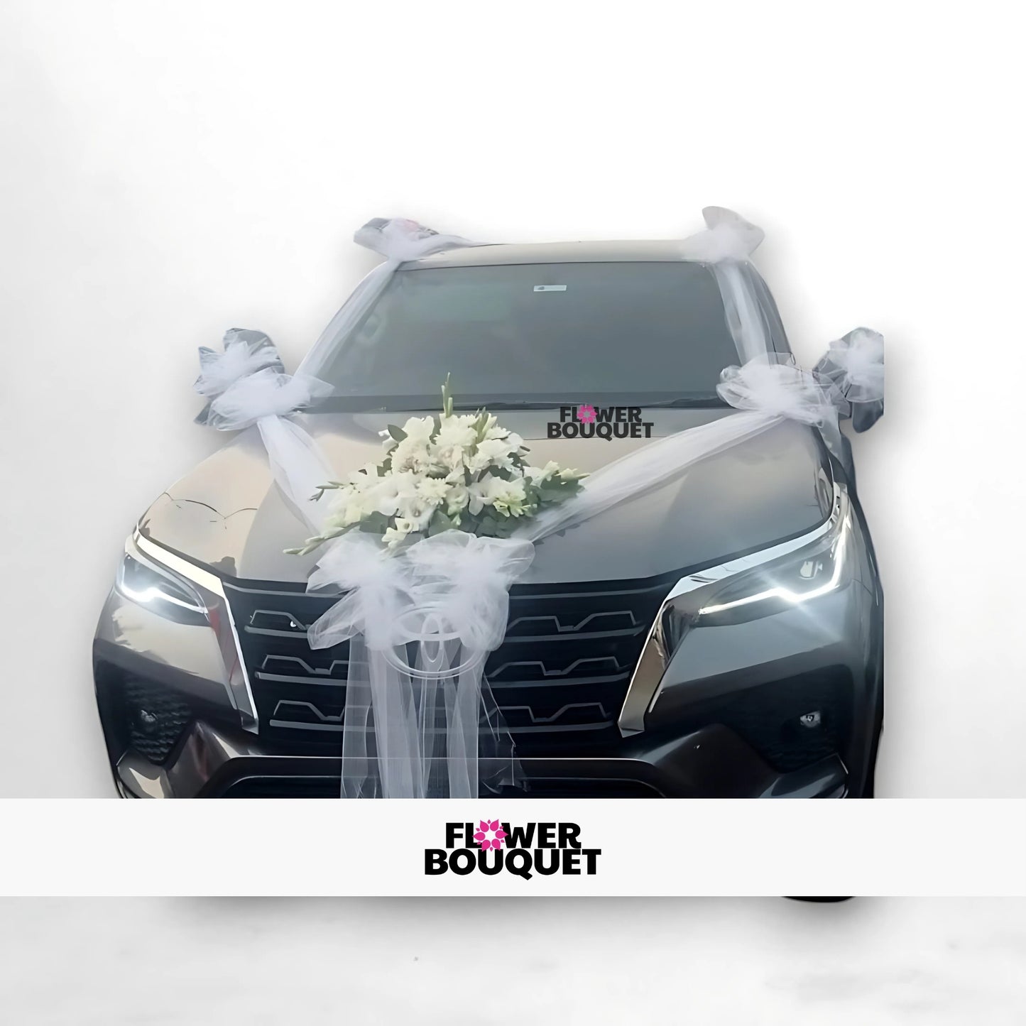 White car decorated with white tulle ribbons and a bouquet of white flowers on the hood.