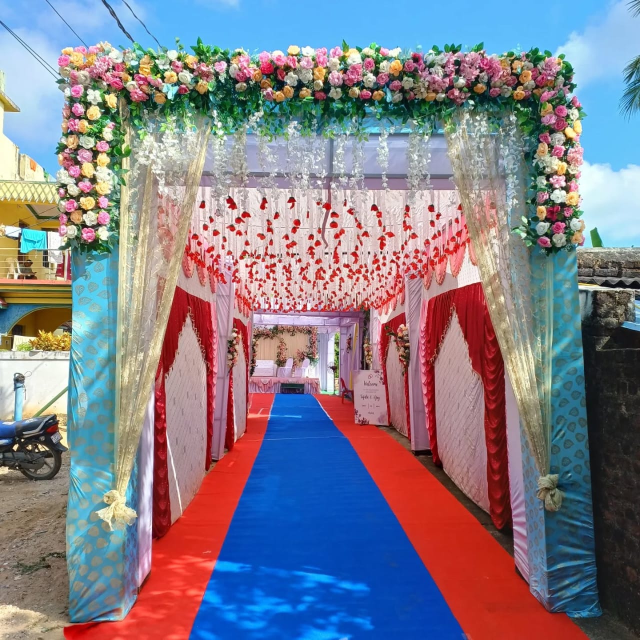 Floral entrance tunnel with colorful flowers, drapes, and a red carpet.