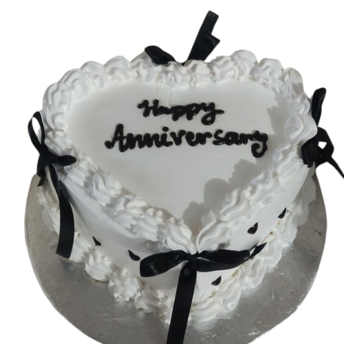 Heart-shaped anniversary cake with white cream frosting and black ribbon decoration.
