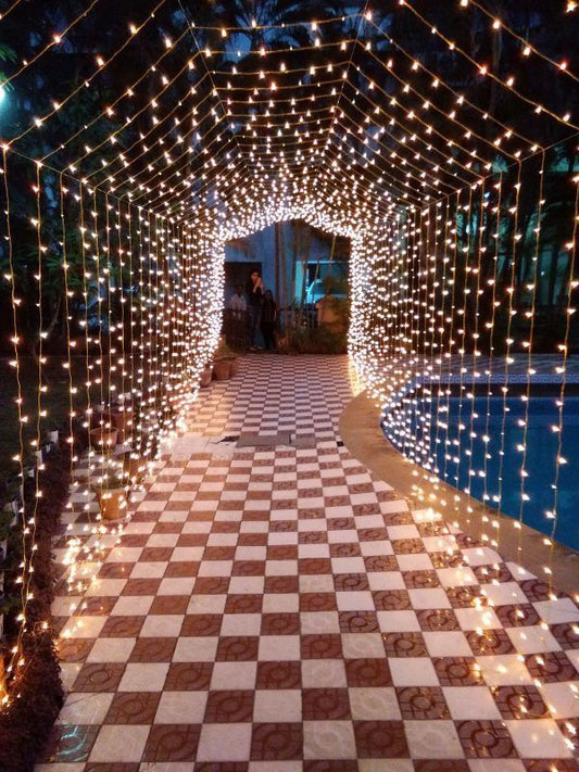 A glowing tunnel made of string lights over a tiled pathway, creating a magical atmosphere for guests to walk through.