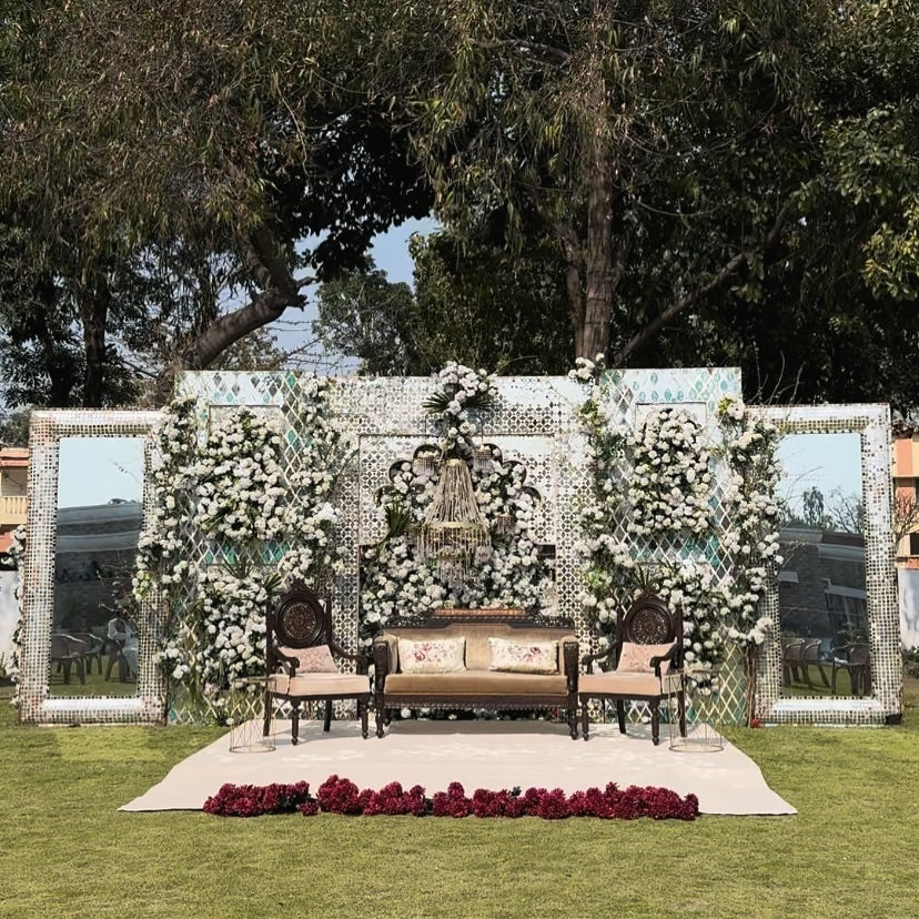 Outdoor vintage wedding stage with antique wooden sofa set, floral walls, and mirrors.