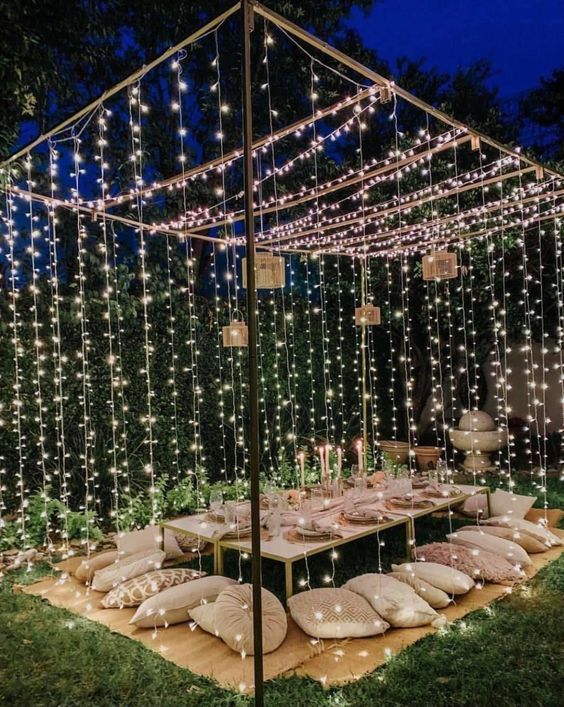 A romantic outdoor dining area with string lights draped above, creating a glowing atmosphere around the table and seating.