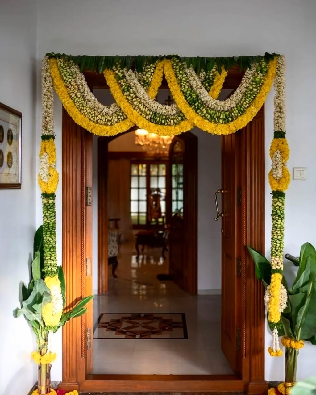 Traditional doorway decoration with marigold and jasmine garlands, banana leaves, and floral pillars on either side.