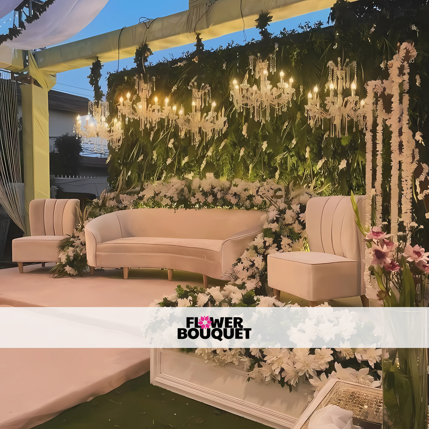 Wedding stage featuring a green backdrop with white floral arrangements, crystal chandeliers, a white curved sofa, and matching chairs, perfect for outdoor events.