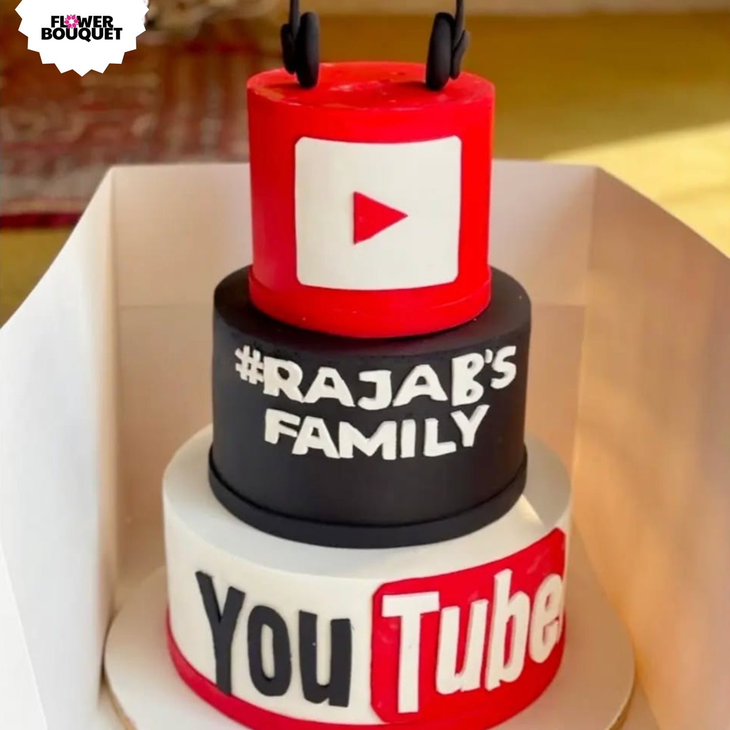 Three-tier YouTube-themed cake with logo, family channel name, play button, and headphones topper.