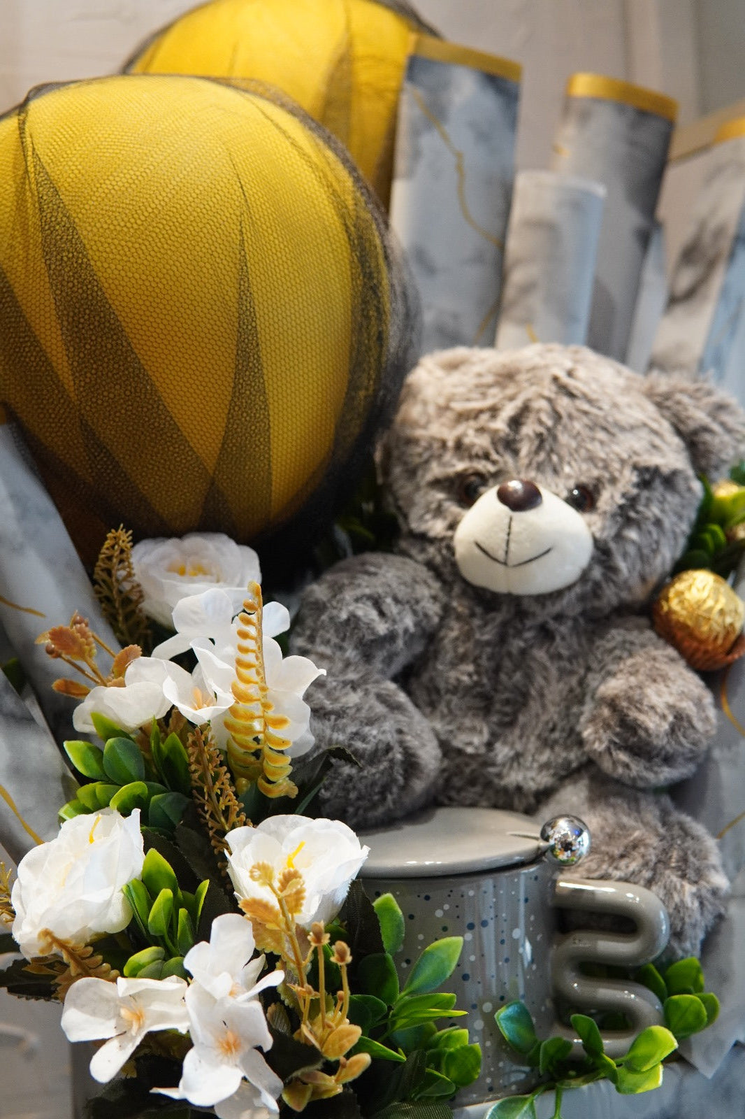 Marble-effect gift box with grey teddy bear, Ferrero chocolates, gold balloon decor, and white flowers – perfect for luxury gifting in Pakistan