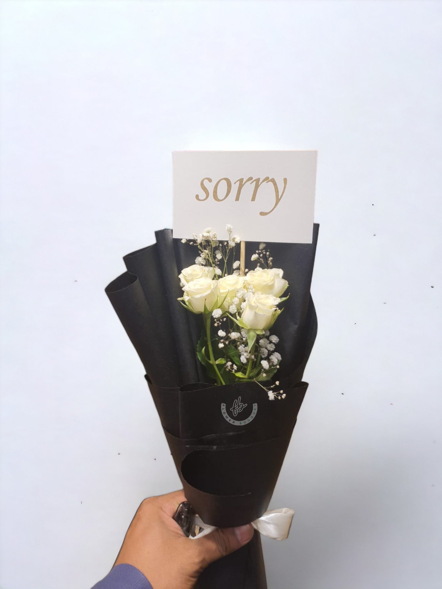 white roses sorry flower bouquet with apology card in it with black wrapping.