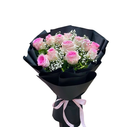 A bouquet of premium pink bi-color roses and white baby's breath wrapped in elegant black matte paper tied with a pink ribbon.
