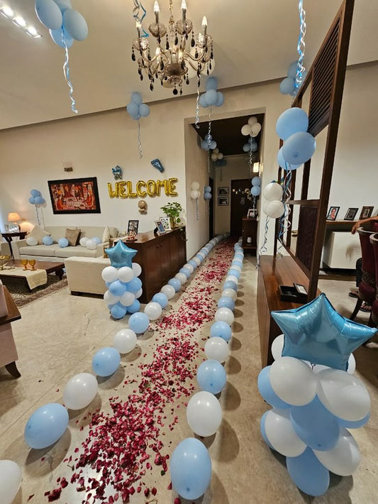 Baby shower entrance decoration with balloons, welcome foil letters, rose petal walkway, and pastel star balloons.
