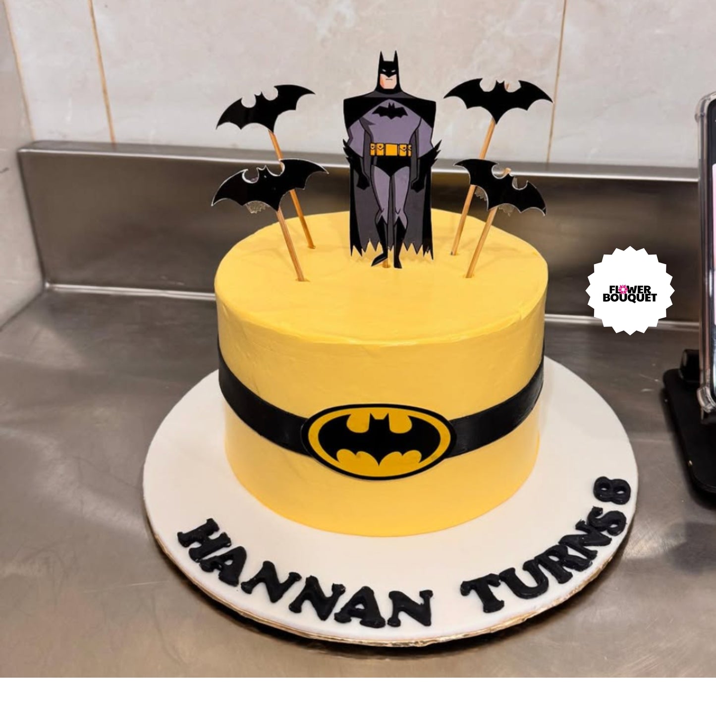 Yellow Batman-themed cake with Batman figure on top, black bat decorations, and Batman logo belt around the middle.