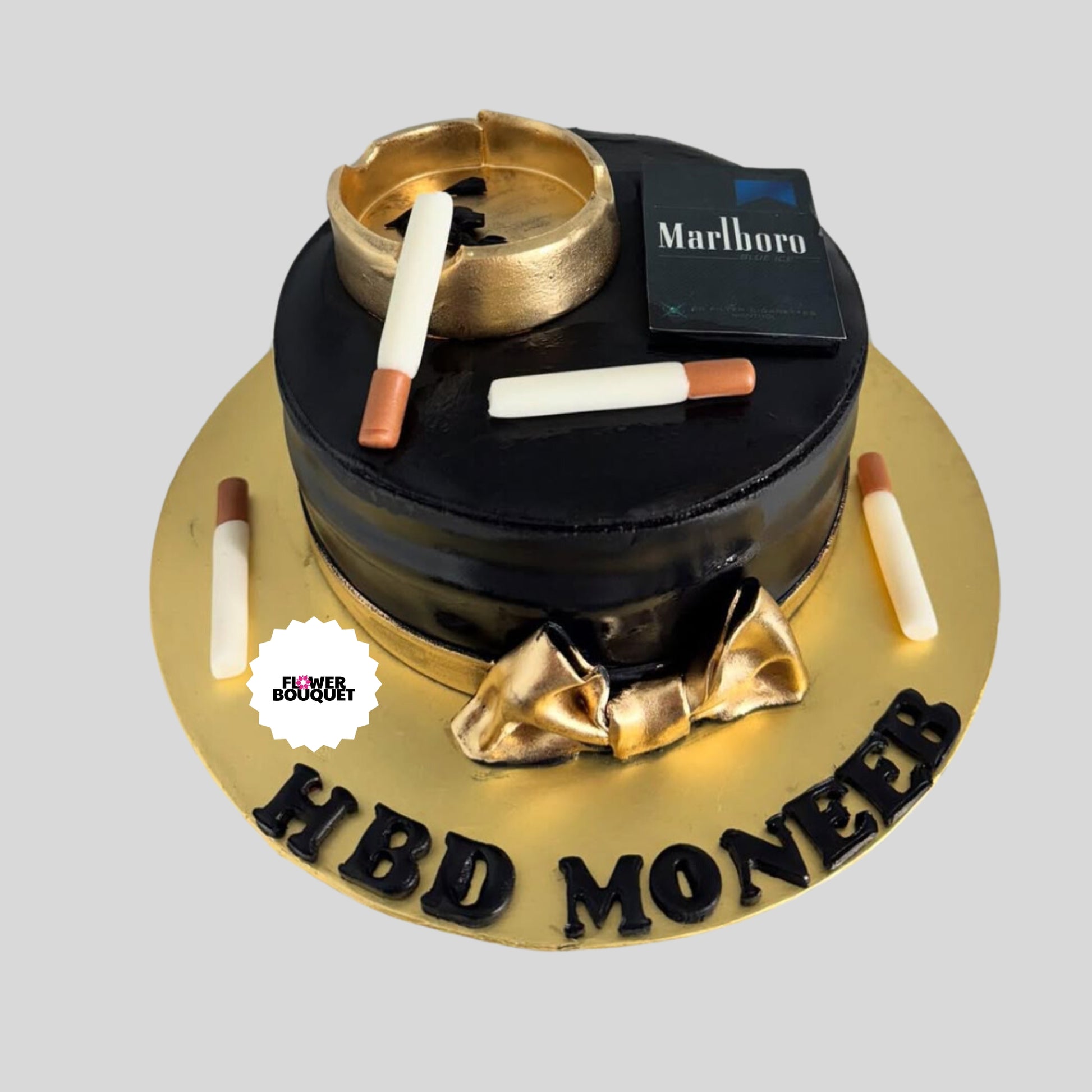 Luxury smoking-themed celebration cake with golden ashtray, lit cigarette, black fondant, and personalized 'HBDMONZER' inscription.