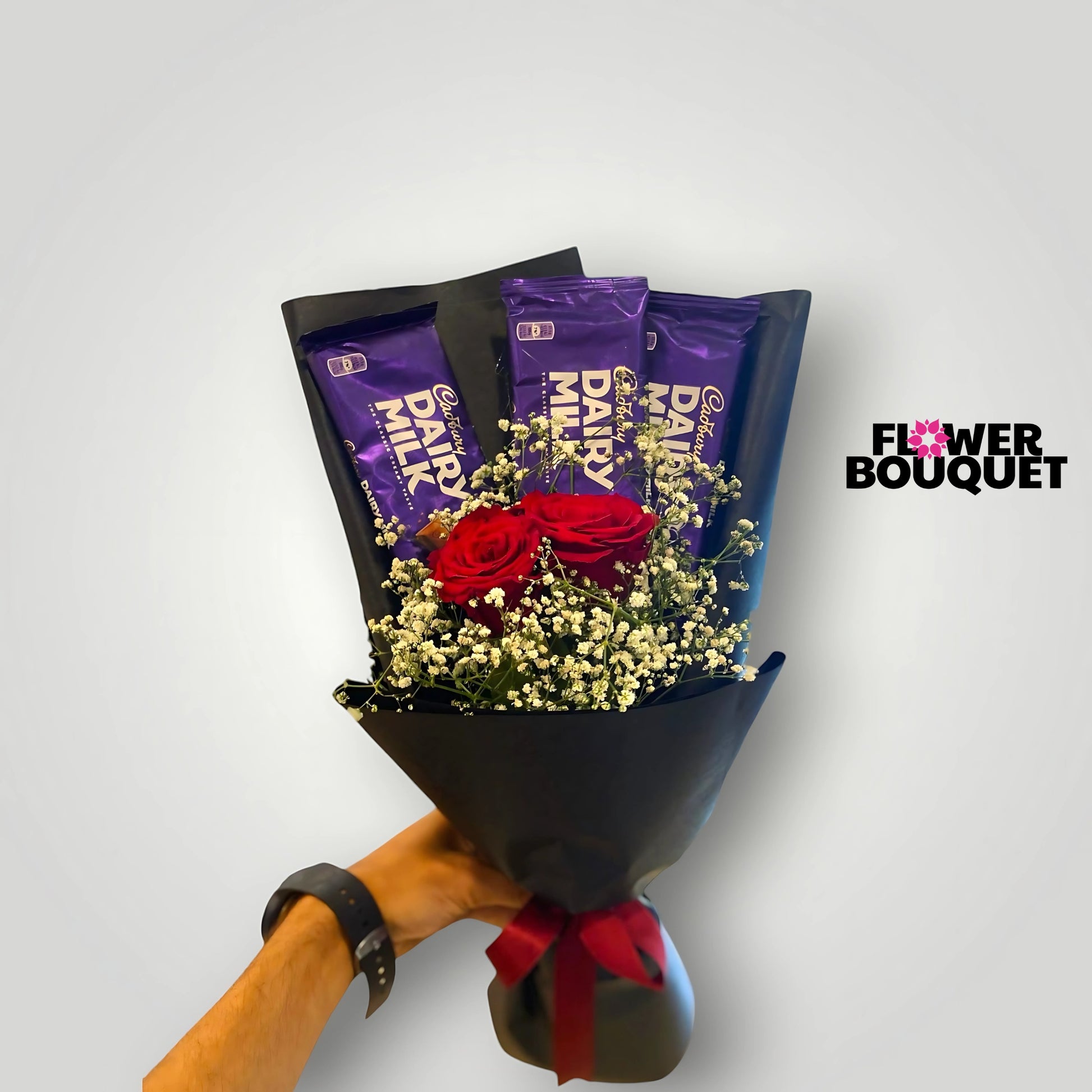 A stunning bouquet featuring vibrant red roses nestled among delicate baby's breath, accented with rich, purple-wrapped Dairy Milk chocolate bars, all wrapped in a sleek black paper for a sophisticated and indulgent presentation.