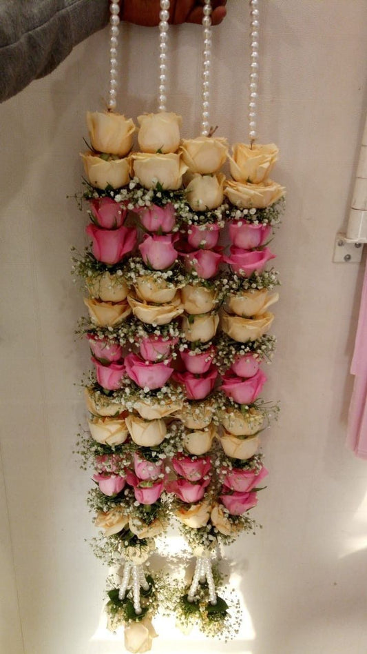 A floral necklace made with pink and white roses, worn for a wedding or special event.