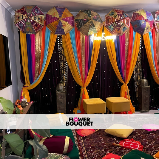 Mehndi decor with vibrant umbrellas, colorful drapes, and a sparkling black backdrop, complemented by cozy seating and traditional decor elements.