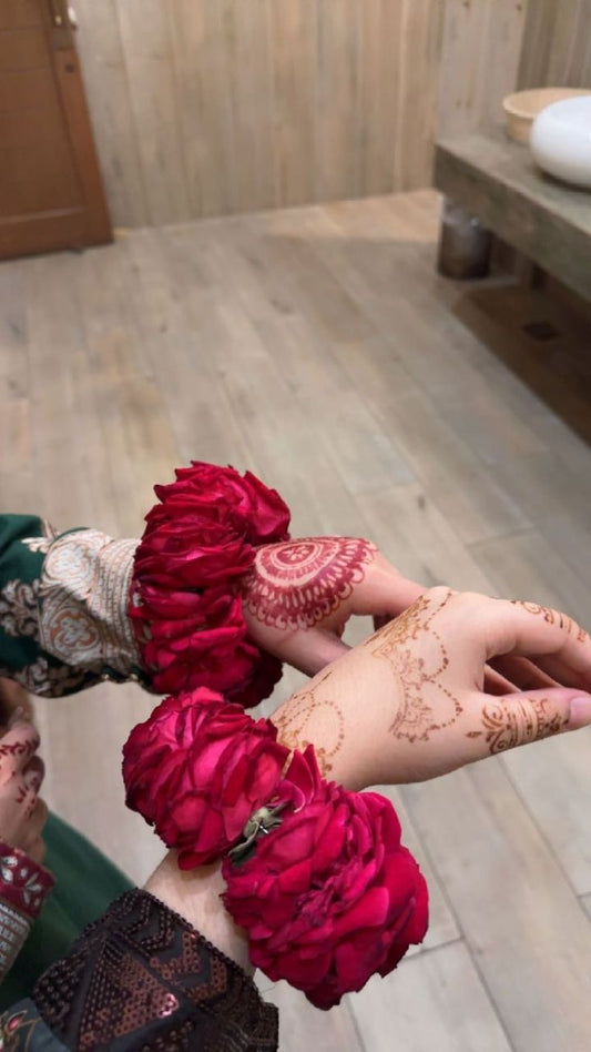 A pair of wrist cuffs made with red roses and baby’s breath flowers, worn during a bridal henna ceremony.

