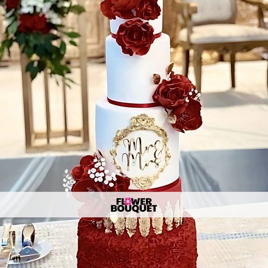 Four-tier wedding cake with white fondant, red edible roses, gold accents, and a custom monogram frame, perfect for elegant weddings.