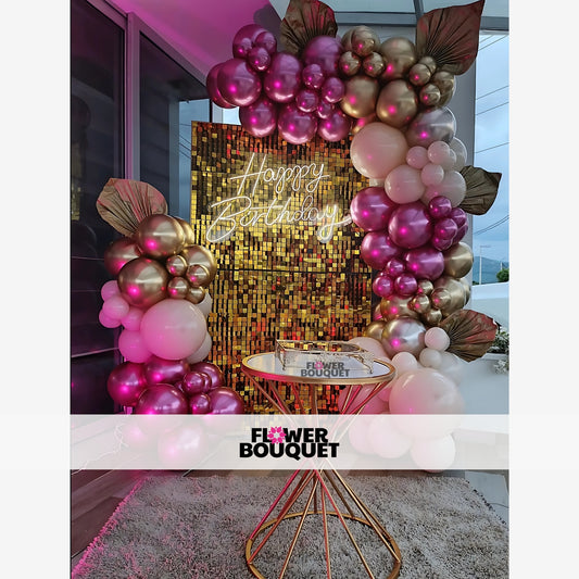 Decorative setup for a birthday celebration with a gold sequin wall, neon "Happy Birthday" sign, and balloon clusters.