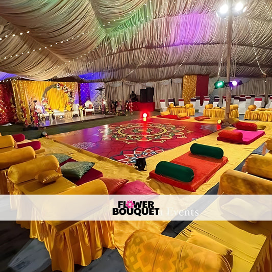 Grand Mehndi decor with a colorful stage, ornate floor designs, cozy seating in yellow and red tones, and detailed lighting for a festive atmosphere.
