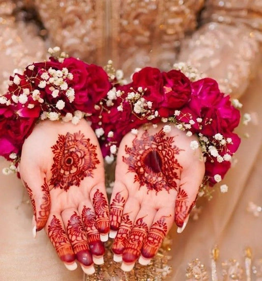 Wrist cuffs made with red roses and baby’s breath flowers, worn during a bridal henna ceremony.