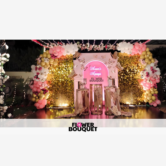 Decorative setup for an event with a gold sequin wall, neon sign, and balloon arch.