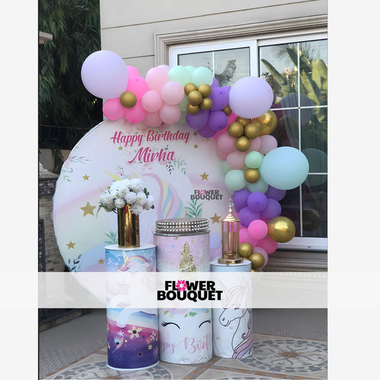 Birthday party setup with a unicorn theme, featuring a circular backdrop, pastel balloons, and decorative stands.