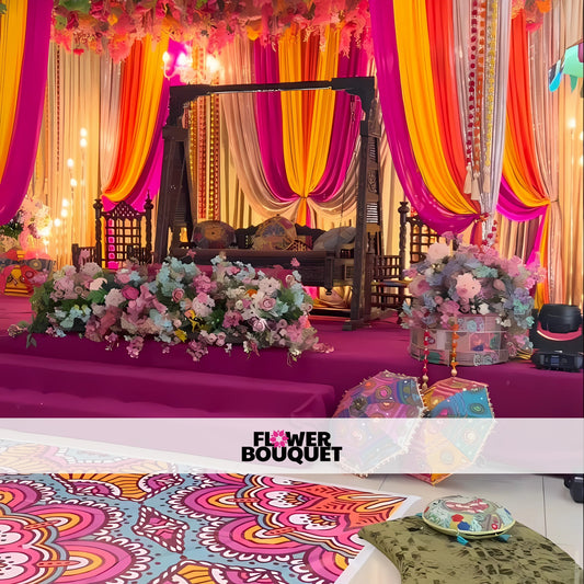 Mehndi stage with vibrant pink, orange, and yellow drapes, a traditional wooden swing, lush floral arrangements, and colorful floor decor for a regal celebration.