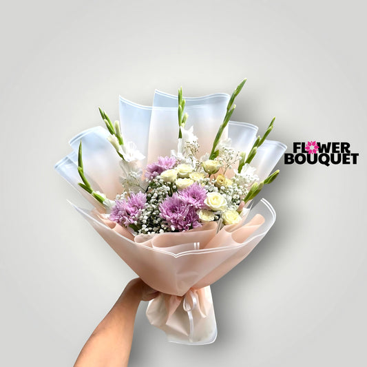 A beautiful bouquet of pastel-colored flowers, including pink chrysanthemums and white roses, arranged in a harmonious and elegant composition and wrapped in a sheer, pale pink fabric.