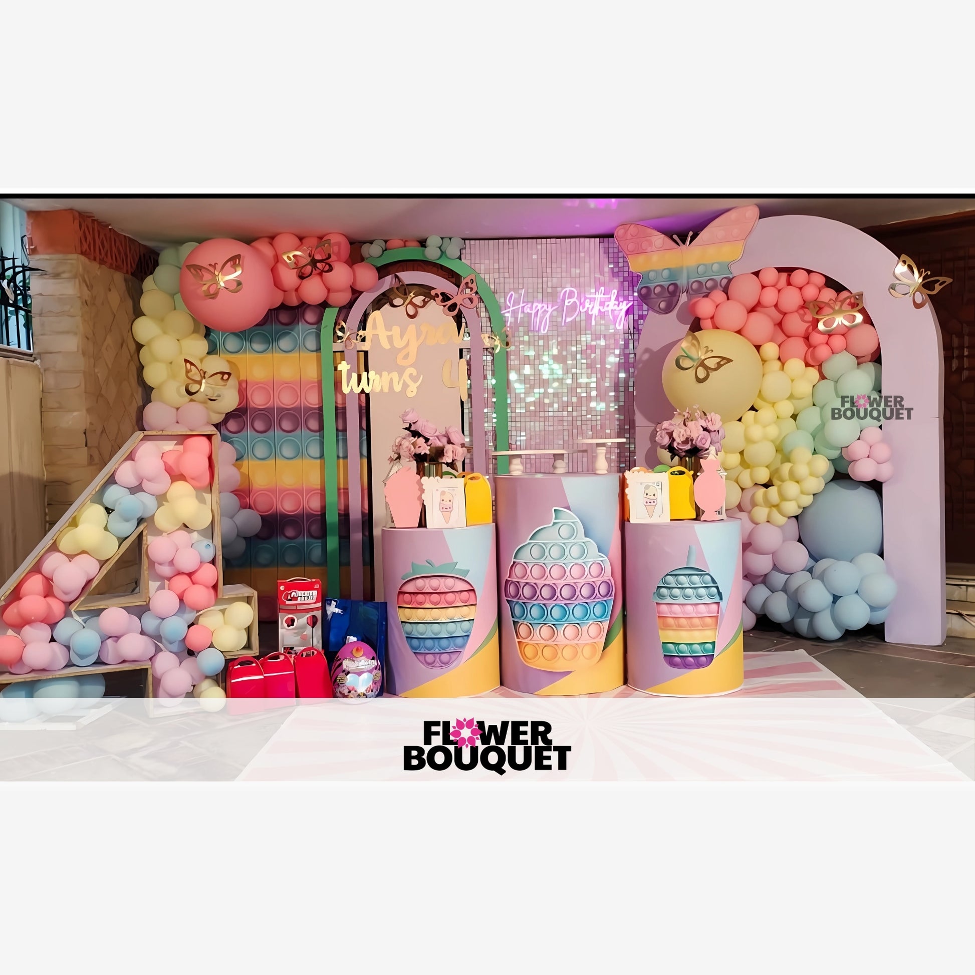 Colorful birthday party setup with a pastel theme, featuring a large number "4" made of balloons, balloon arrangements, and pop-it toys.