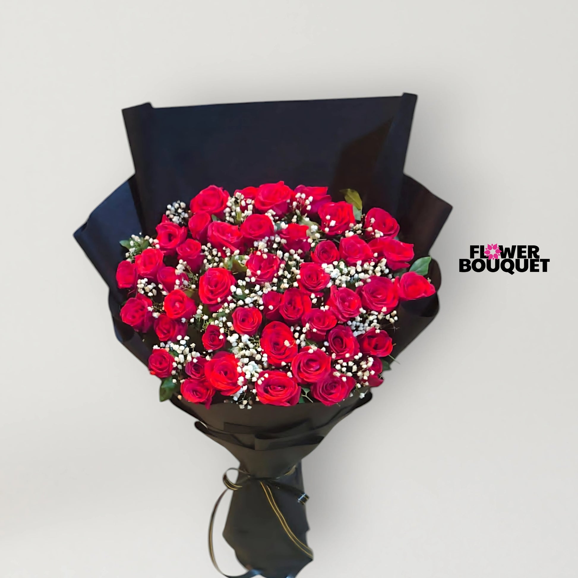 A large, luxurious bouquet of deep red roses with baby's breath, wrapped in sleek black paper.